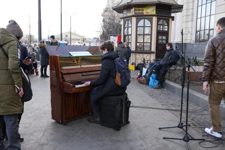 Eine Wissenschaftlerin und ein Wissenschaftler arbeiten hinter einer Glasfassade und mischen Chemikalien mit Großgeräten.